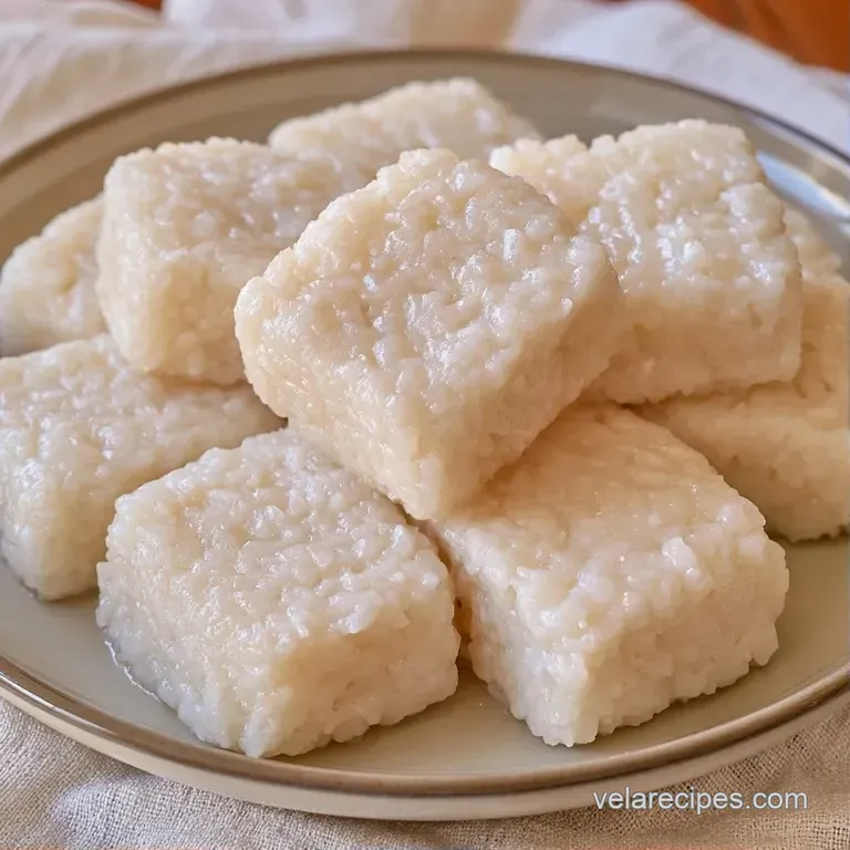 Translucent white rice cubes arranged neatly on a dark platter, drizzled with thick, creamy white coconut cream.