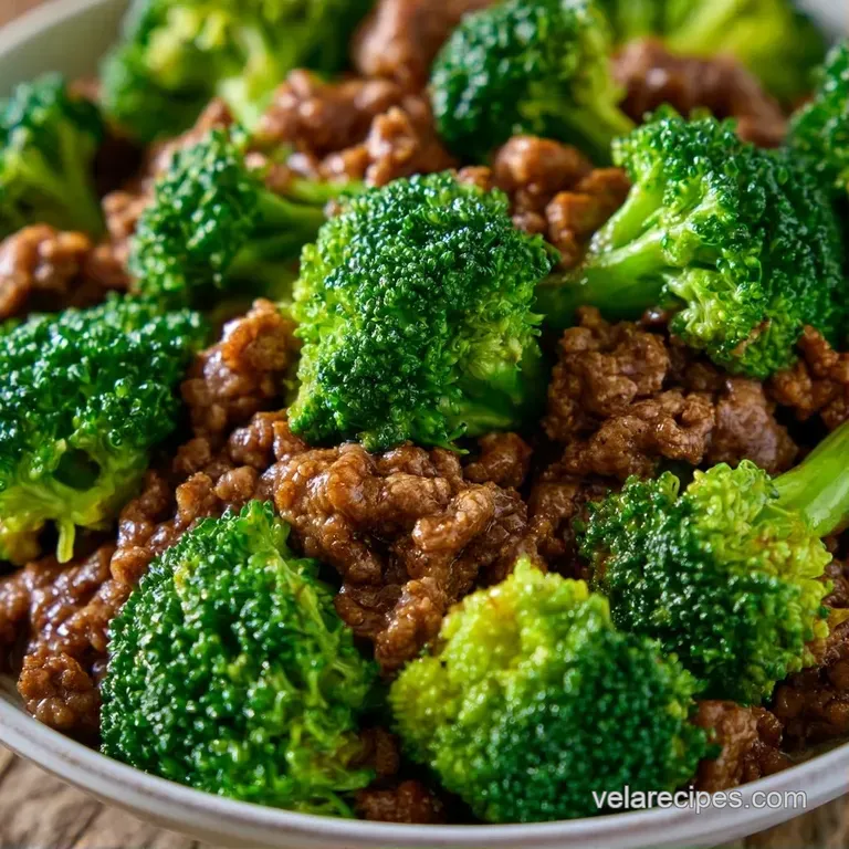 Glistening brown beef and vibrant green broccoli topped with sliced scallions in a white bowl on a wooden table.